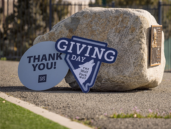 A &ldquo;Giving Day&rdquo; sign and a &ldquo;Thank you!&rdquo; sign lean against a large rock outdoors. 