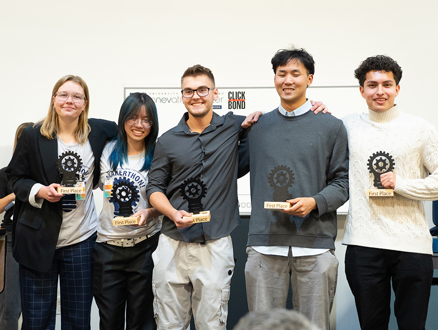 A group of five people stands together, smiling, each holding a "First Place" award.