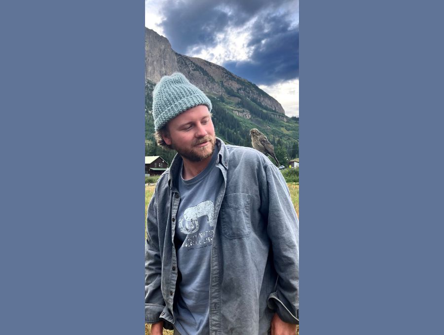 David outside in the mountains with a small, wild bird perched on his shoulder.