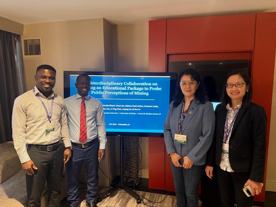 Four individuals standing next to a presentation screen wearing business attire and smiling.
