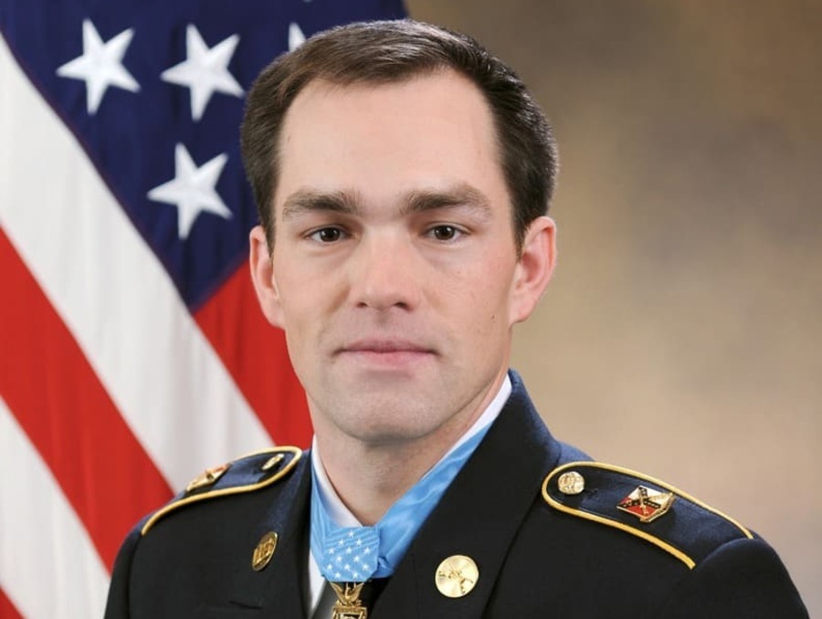 Clinton Romesha in military attire, with American flag in background.