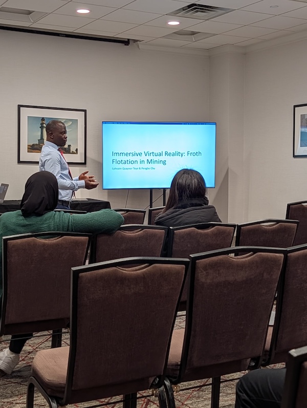 A man presenting to an audience during a conference with a presentation titled "Immersive Virtual Reality: Froth Flotation in Mining."