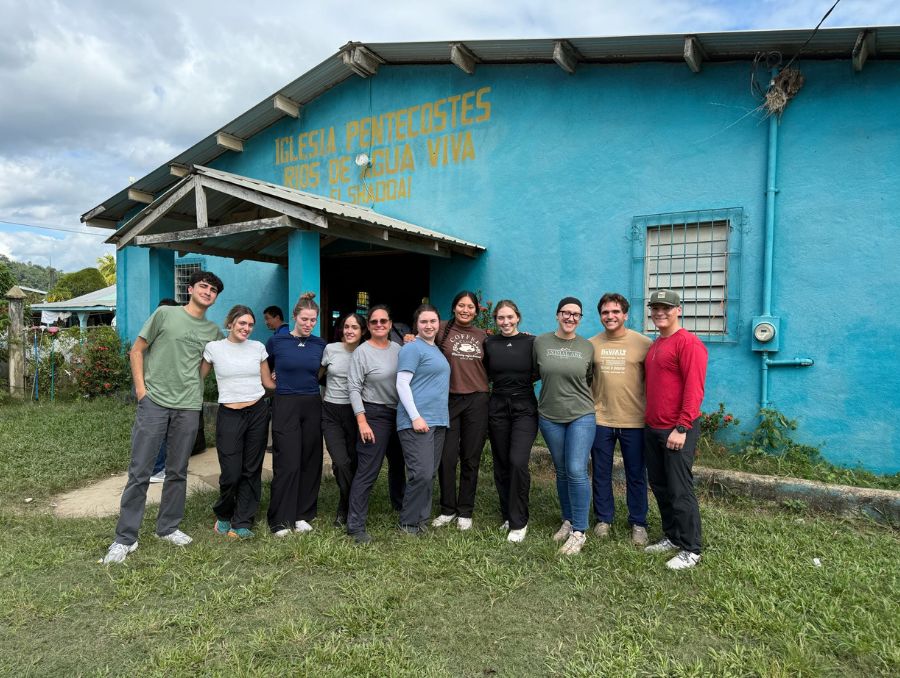 The group of students and faculty in Belize standing in front of a bule building.