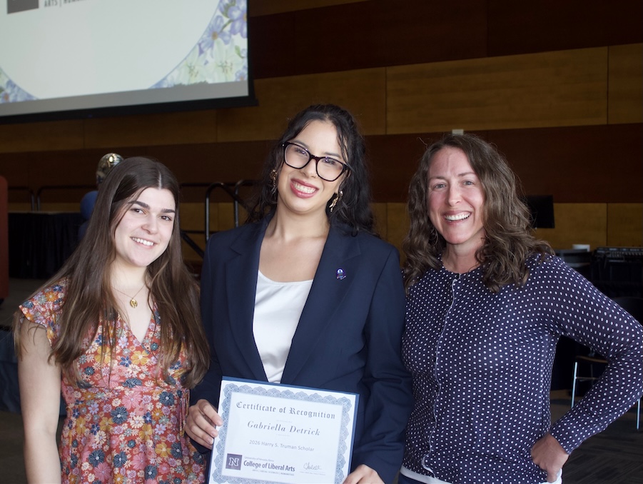Three women standing together at an awards ceremony. Gabby, in the middle, holds a certificate for being a Truman Scholar. 