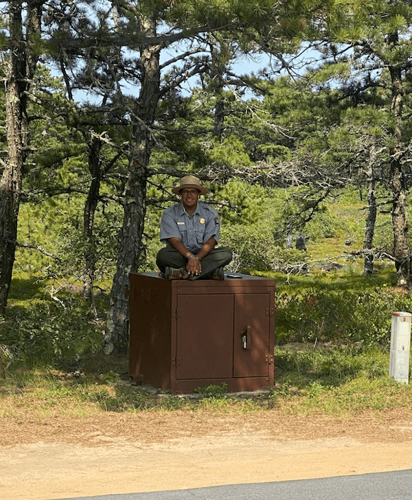 Grayson in a park ranger uniform, sitting atop a bear-safe box outside.