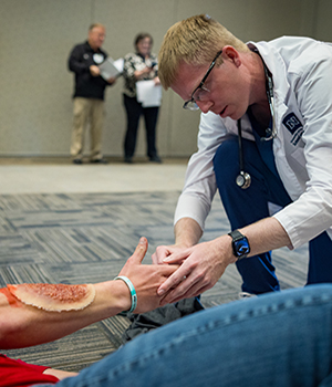 A medical student assesses a simulated patient with an arm wound.