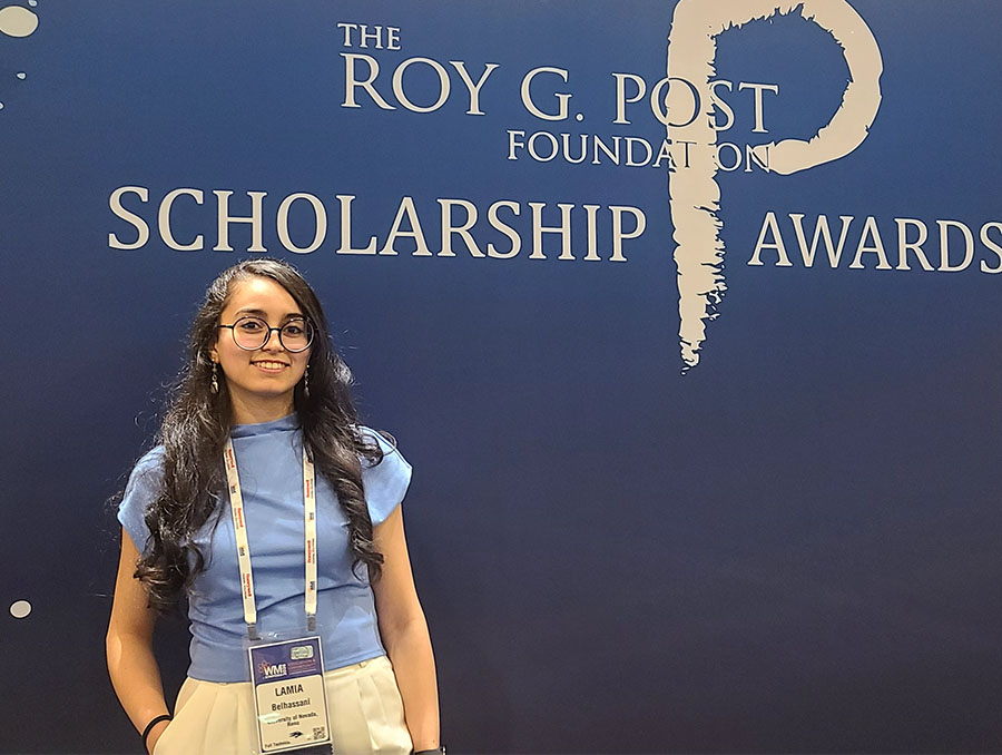 A woman stands in front of a darj blue background that reads "Roy G. Post Foundation Scholarship Awards."