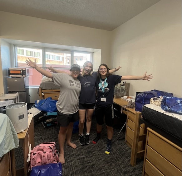 Lauren and two friends standing inside a dorm room, smiling.