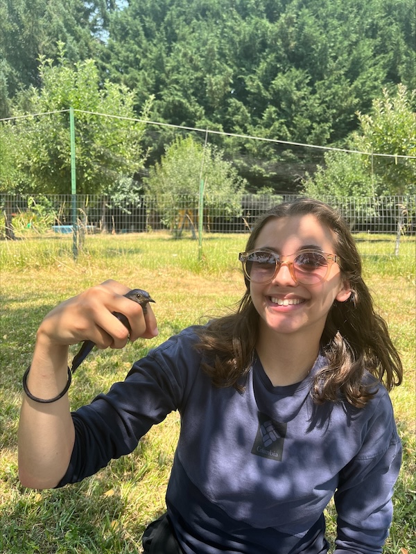 Manon holding her hand out with a small, wild bird perched on her finger in the mountains.