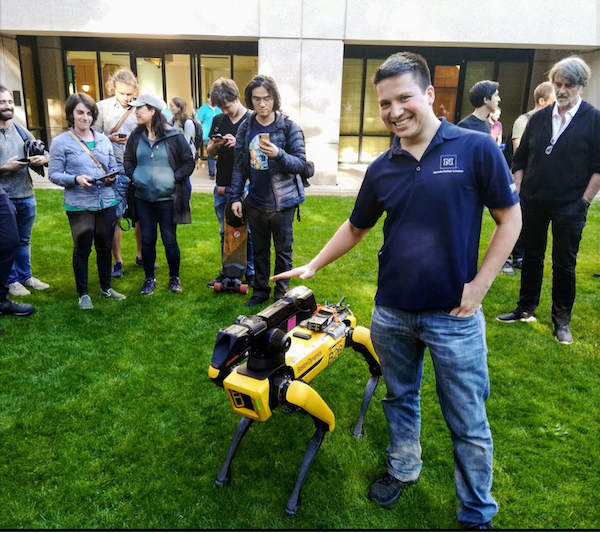 Retana in a Nevada polo, on campus with a robot, with students and faculty gathered around him.