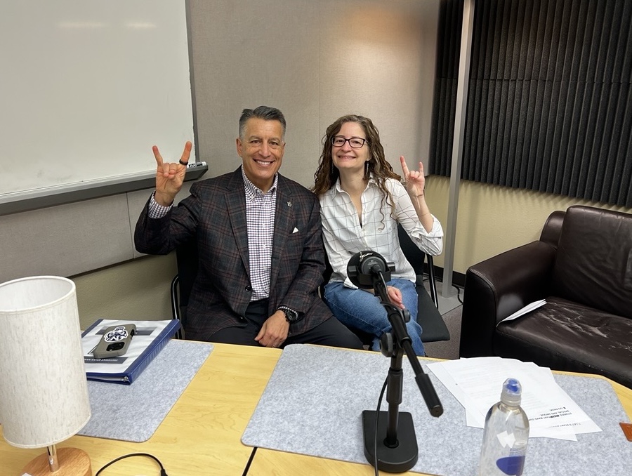 Beth Leger sits next to President Sandoval in the podcast recording studio, while making the Wolf Pack hand sign. 