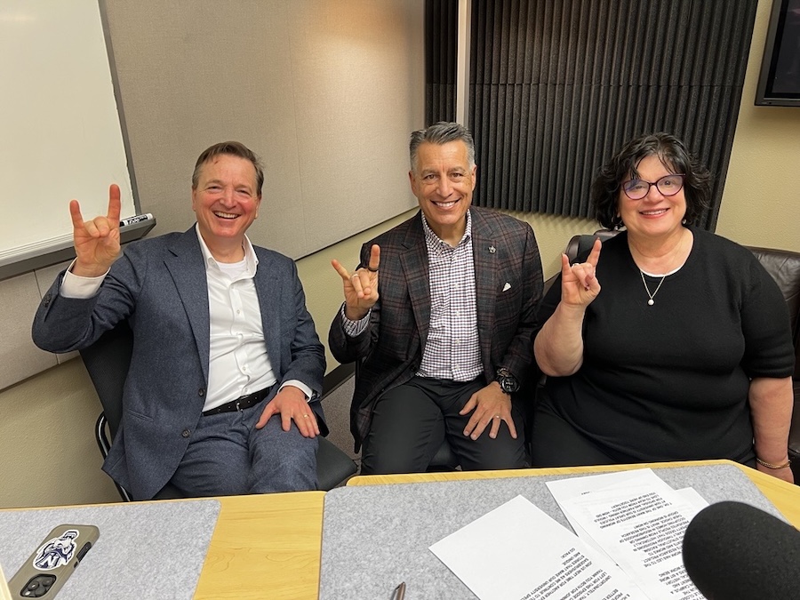 Dr. von Nagy sits next to President Sandoval and Dr. Linda Curcio-Nagy in the podcast recording studio. All hold up Wolf Pack hand signs, smiling. 