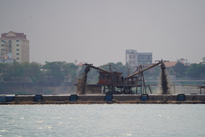 Two crane-looking devices pour sand onto a barge in the middle of a river.