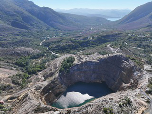 A view of a large and lush valley with an open pit mine below, filled with water.