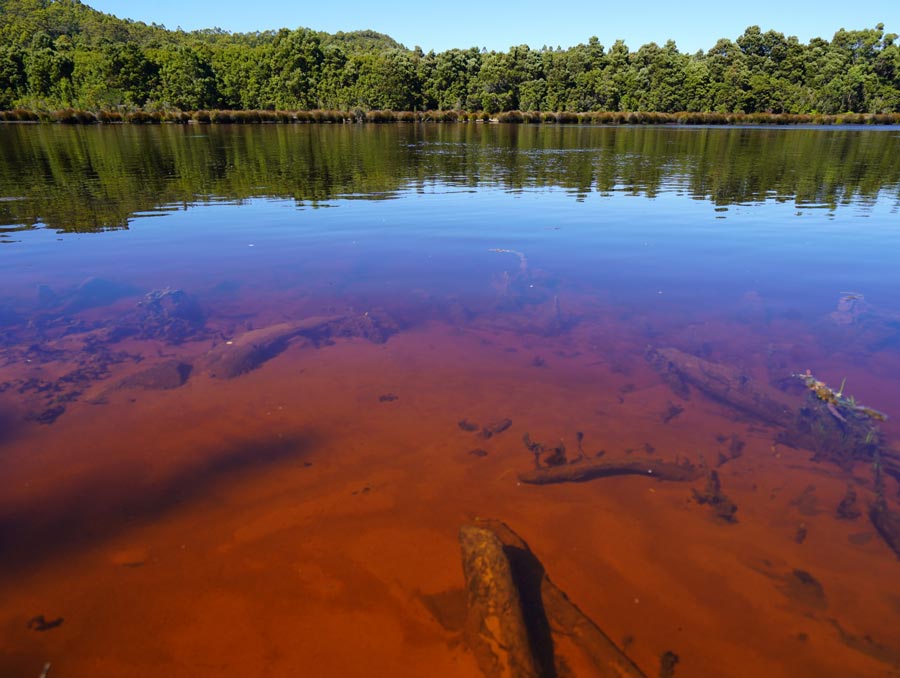 The foreground shows a bright reddish-brown river, with a lush riverbank in the background.