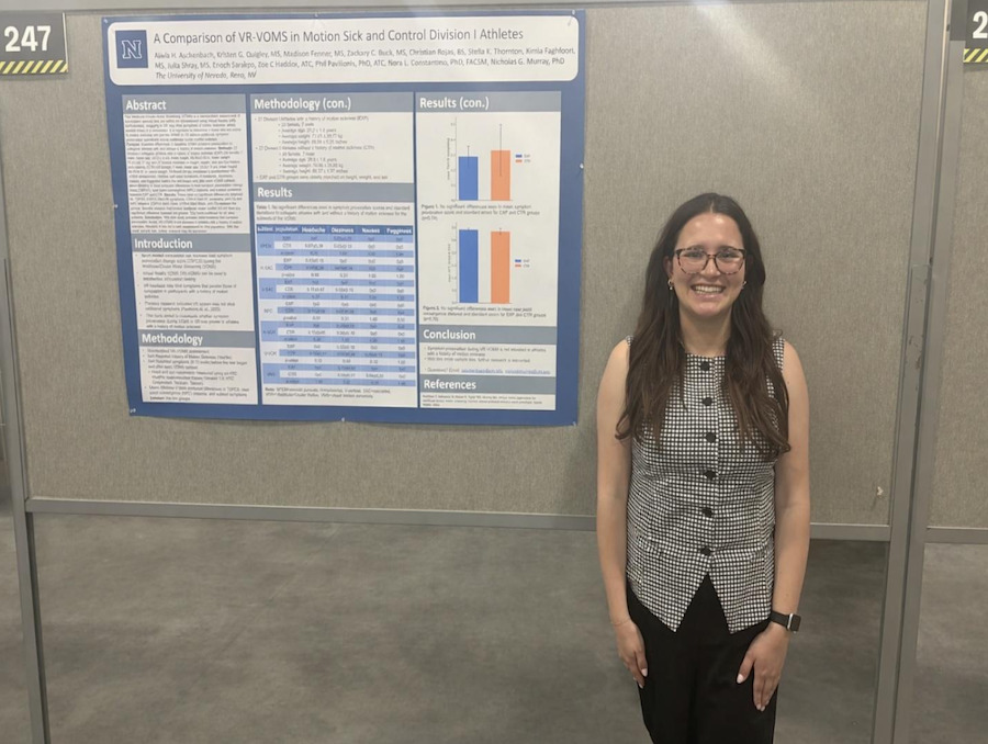 Alivia Aschenbach standing in front of her research poster, smiling.