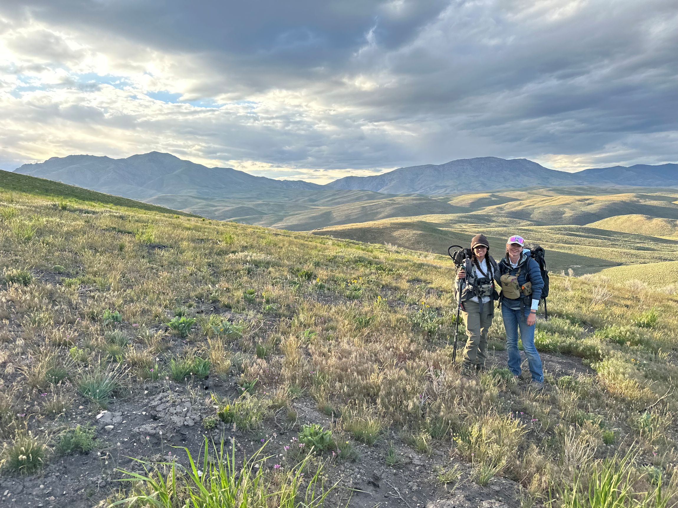 Ava and Sophie dressed in hiking gear walking up a hilly rangeland. 
