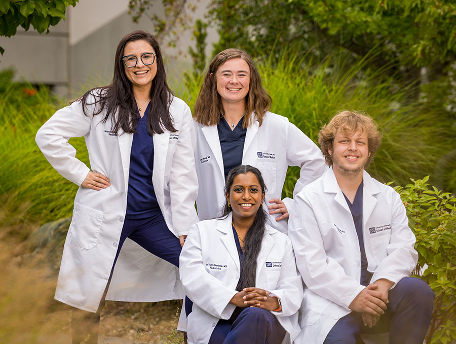 Four pediatrics residents in white coats sitting outside.