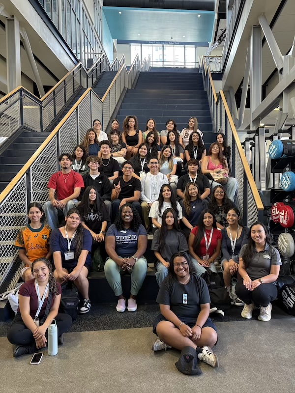 A large group of students posing with Harvey on the stairs at the fitness center during CBESS.