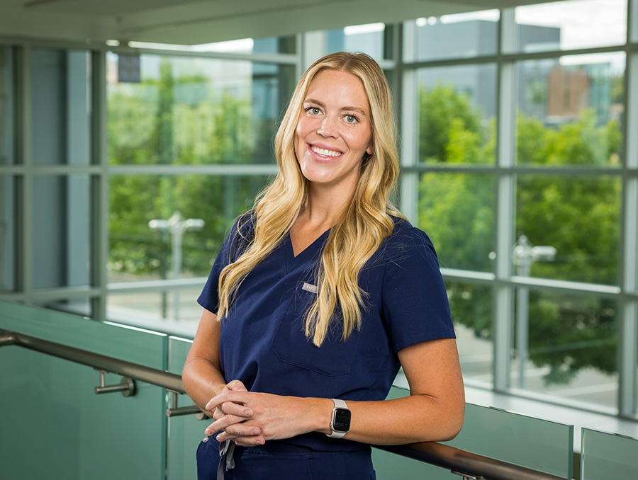 Jennifer Geddes in scrubs standing in a building with glass windows behind her.