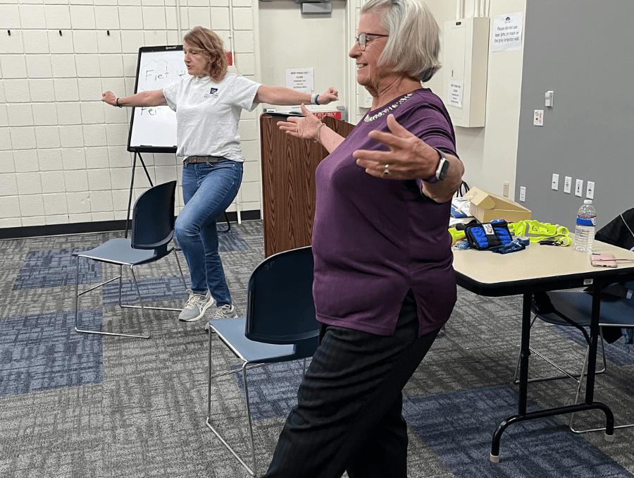 Two women are balancing on one leg with their arms outstretched. 