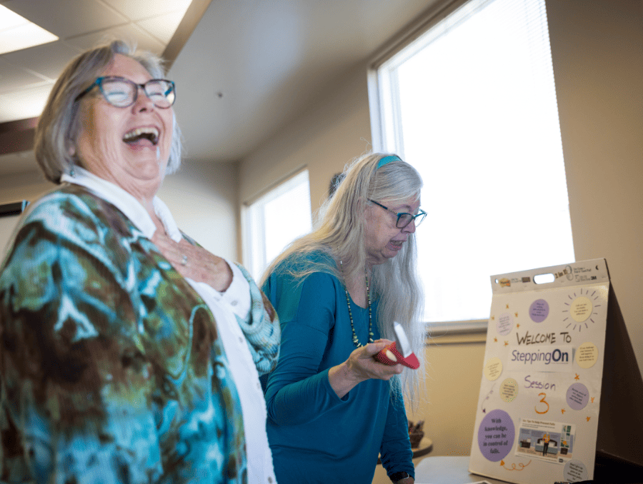 Two older women are laughing while looking at a table.