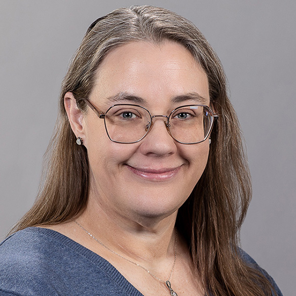Kimberly Andersion sits for a portrait wearing glasses and dark blue v-neck top and necklace.
