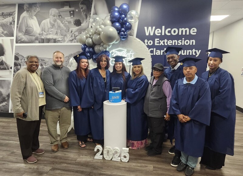 A group of graduates in blue caps and gowns posing with faculty members in front of a sign reading "2025."