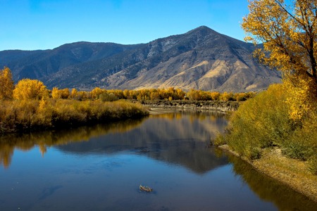 A landscape featuring a calm river reflecting blue skies and surrounded by autumn foliage. 