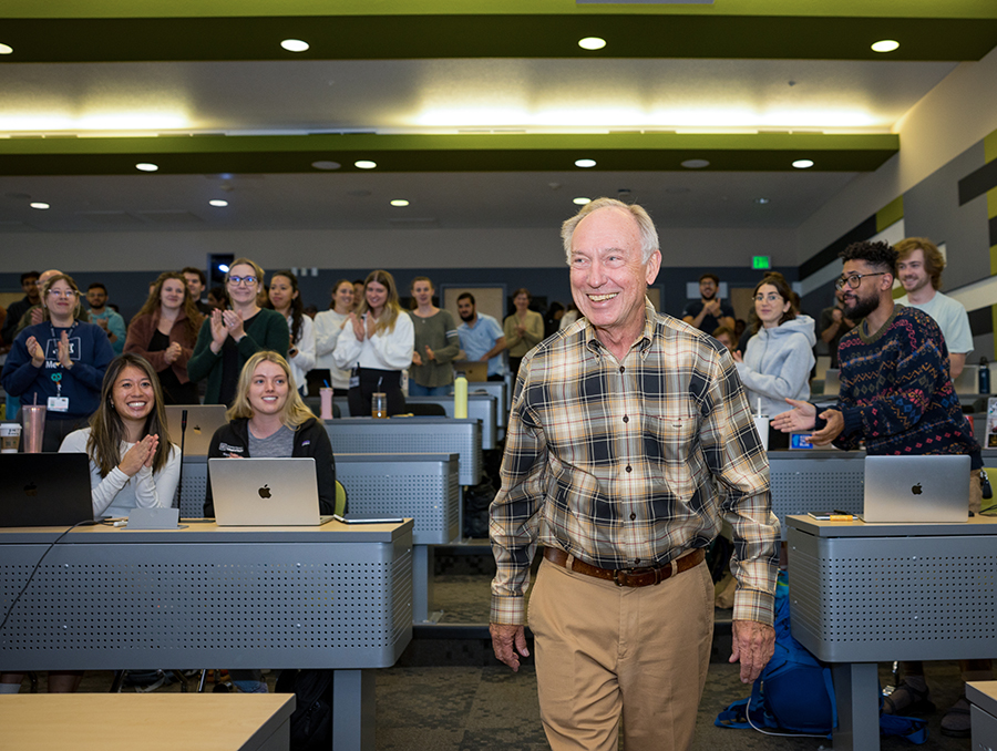 Kozel walking down an aisle in a classroom full of medical students standing and clapping for him.