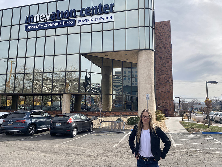 A person stands smiling in a parking lot in front of the Innevation Center, University of Nevada, Reno. Multiple cars are parked nearby, and the building is marked with "Powered by Switch."