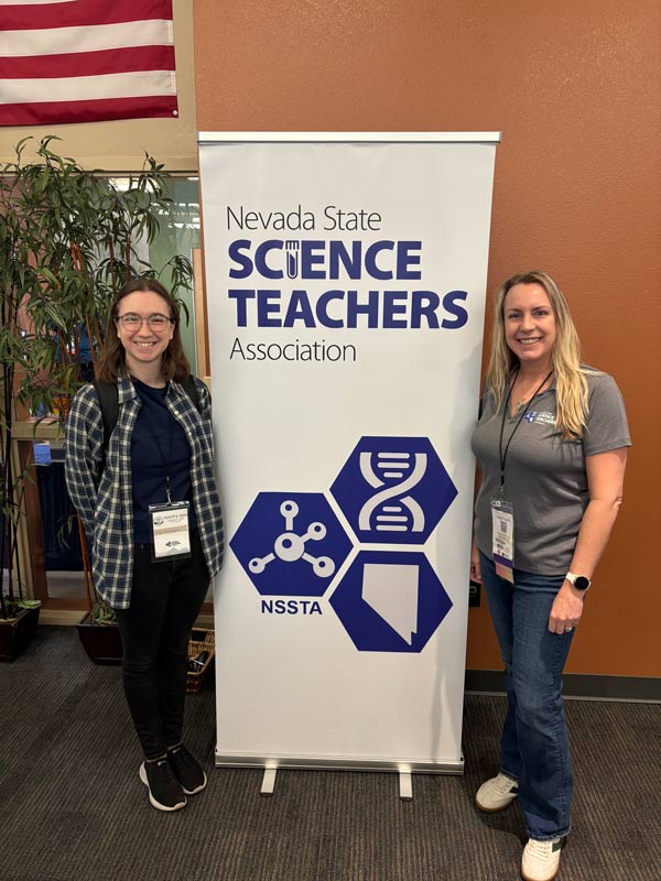 Two people pose with a pop-up banner that reads, "Nevada State Science Teachers Association."