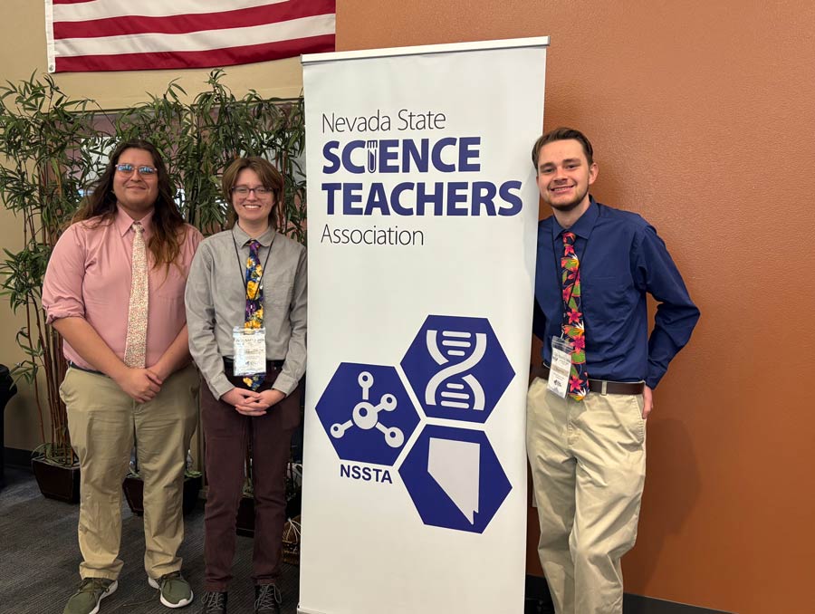 Three people pose with a pop-up banner that reads, "Nevada State Science Teachers Association."