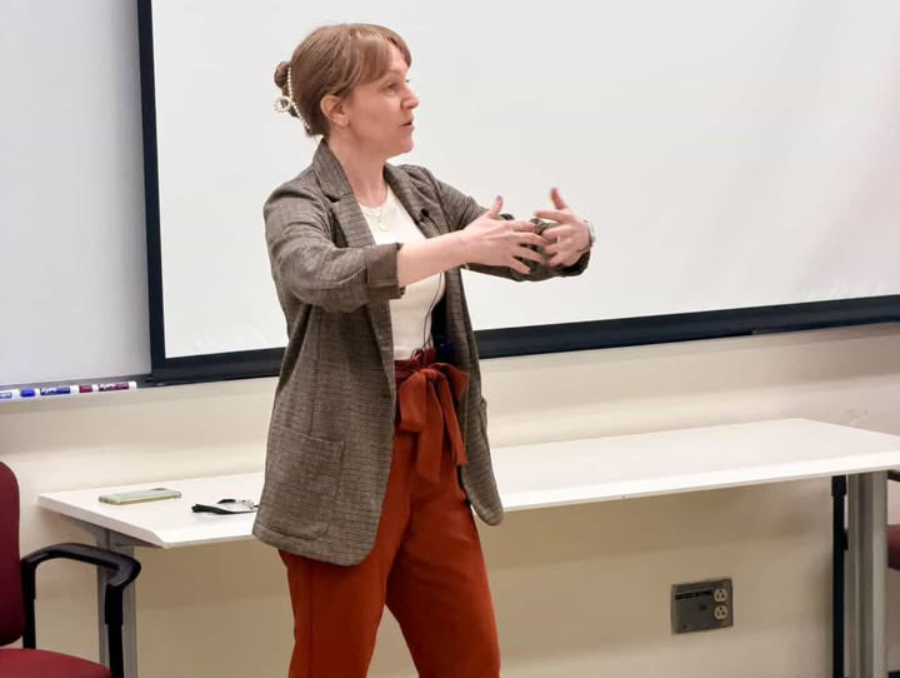 Susanna stadning in front of a classroom, holding her arms in a hoop in front of her.
