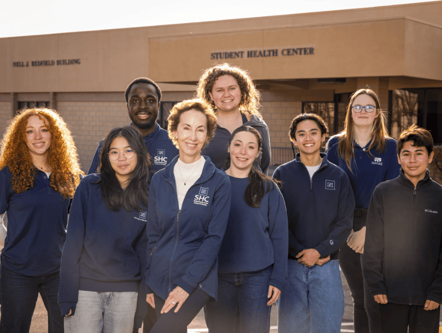 A group of students and faculty standing in front of a building that says "Student Health Center."