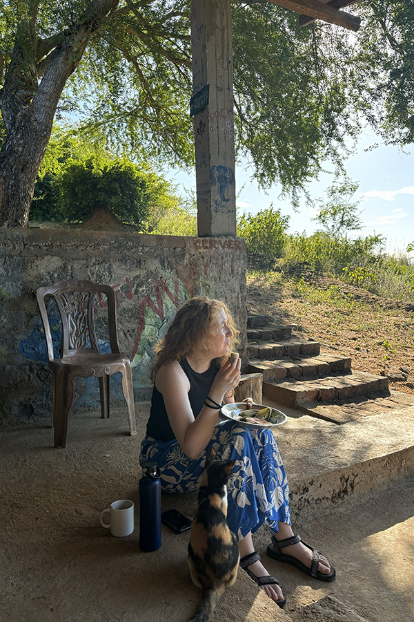 Avery sat on a stone step outdoors eating a meal next to a cat. 