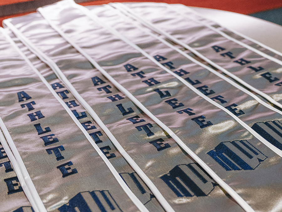 Graduation stoles with text ATHLETE and the Mountain West logo lined up on a table.