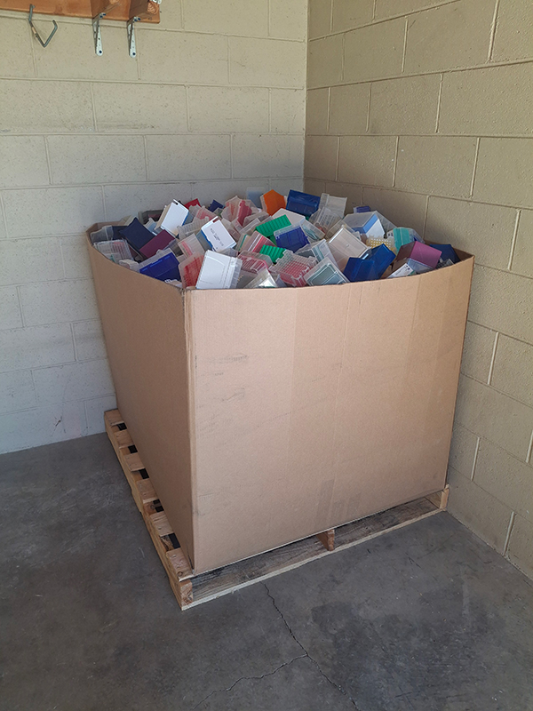 A large brown cardboard box filled with smaller plastic pipette tip boxes in a grey room.