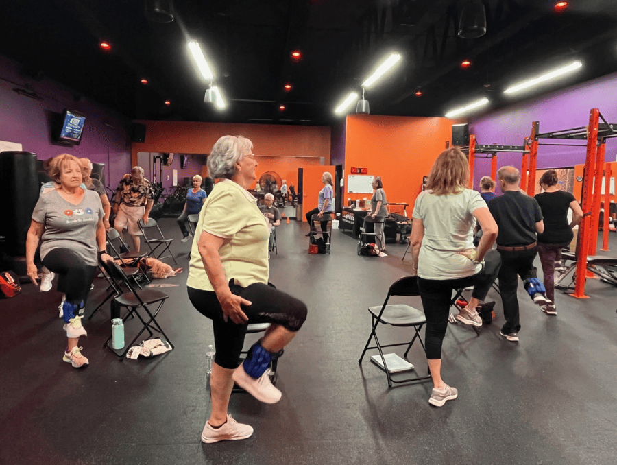 Older adults in a gym are marching in a circle to strengthen their muscles.