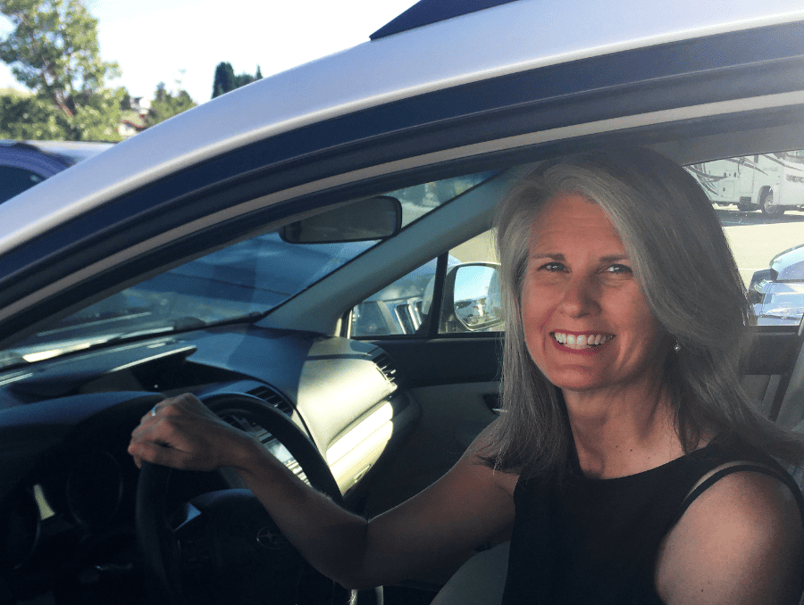 A woman smiling from inside the driver's seat of a car.