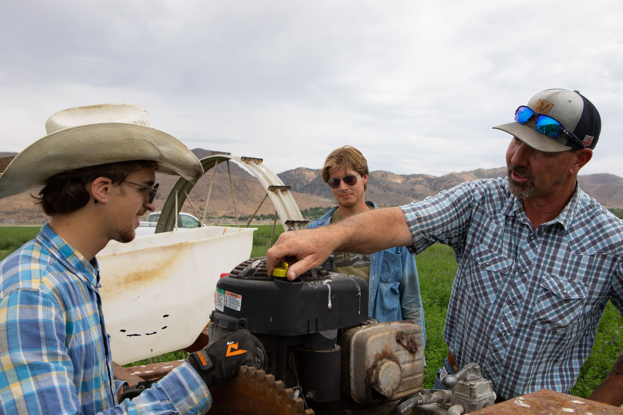 Bo Kindred fine-tuning a farm equipment as two students look on. 