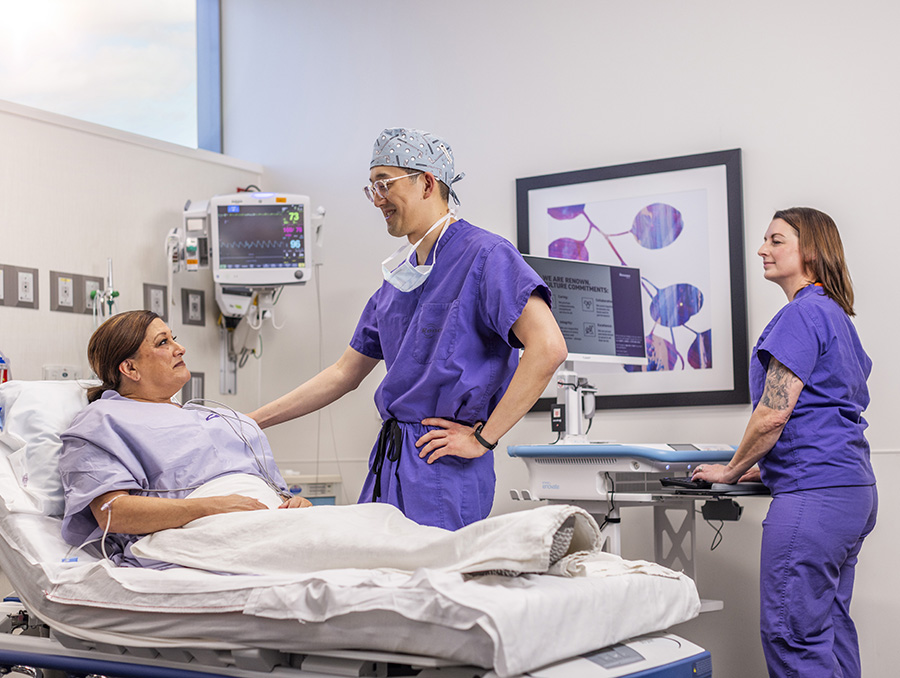 A physician in scrubs talking with a patient in a hospital bed.