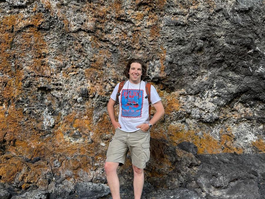 A person stands smiling against a rocky background.