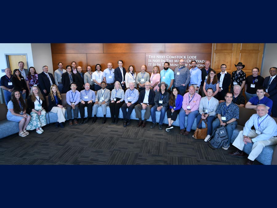 A large group of people, with one row sitting and another row standing behind, smile for a photo in the Joe Crowley Student Union.