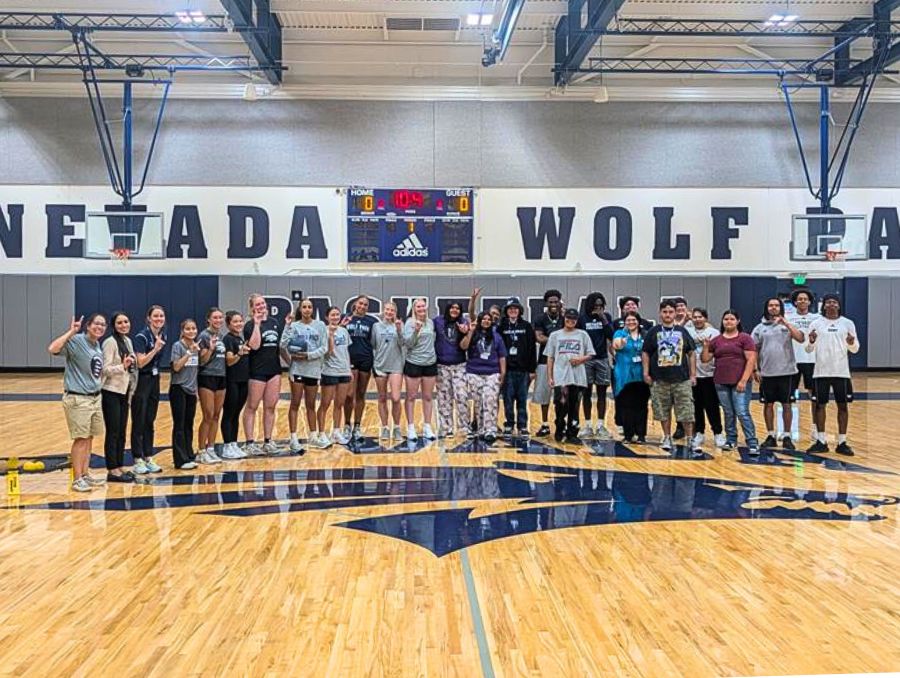 A large group of students smiling and holding Wolf Pack hand signs on a Wolf Pack branded basketball court.