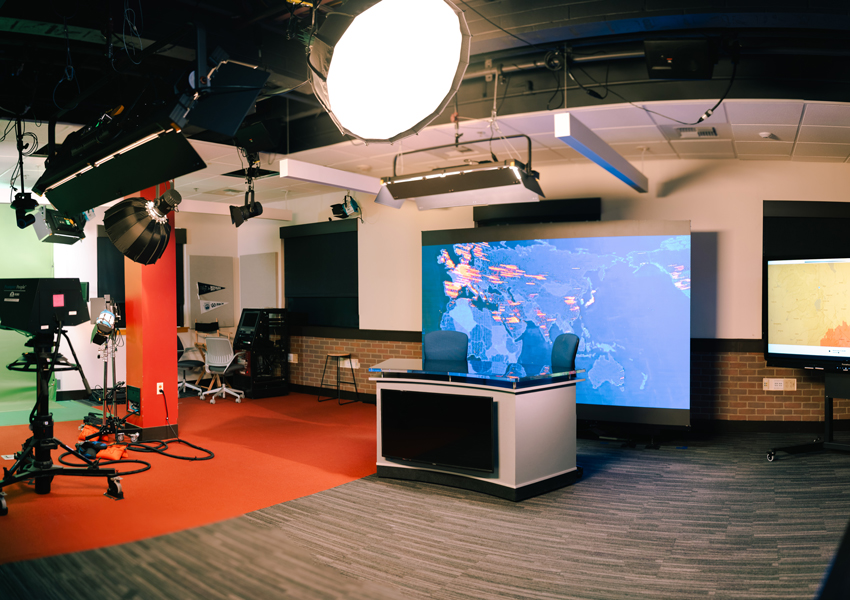 The newsroom, including a formal broadcast desk in front of an LED video wall and the green screen set to the left of it.