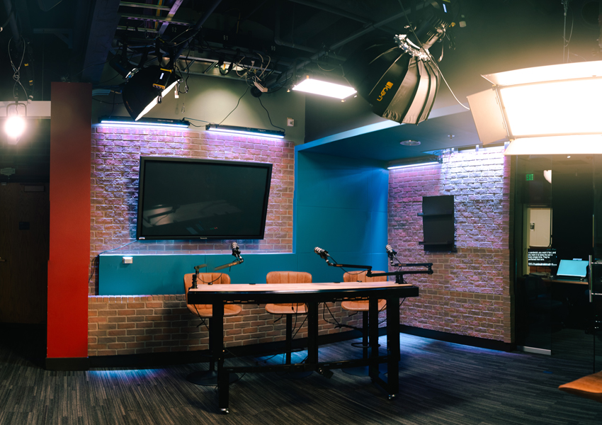 The informal broadcast set surrounded by professional lighting and monitors.