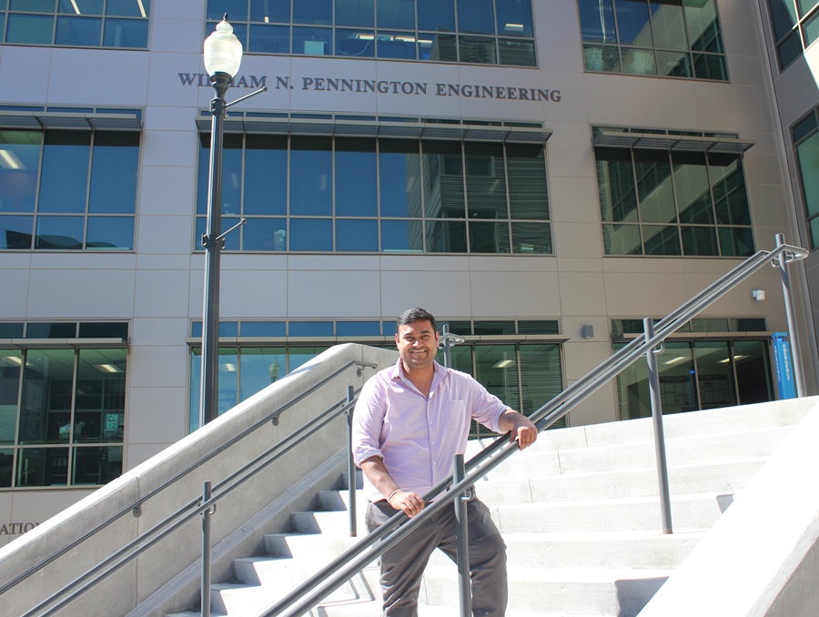 Man standing on outdoor cement stairway, building behind him with letters that read William N. Pennington Engineering.