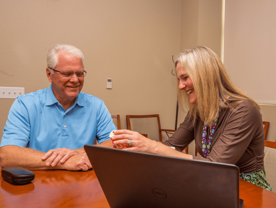 An older man speaks with a woman while looking at prescription bottles.