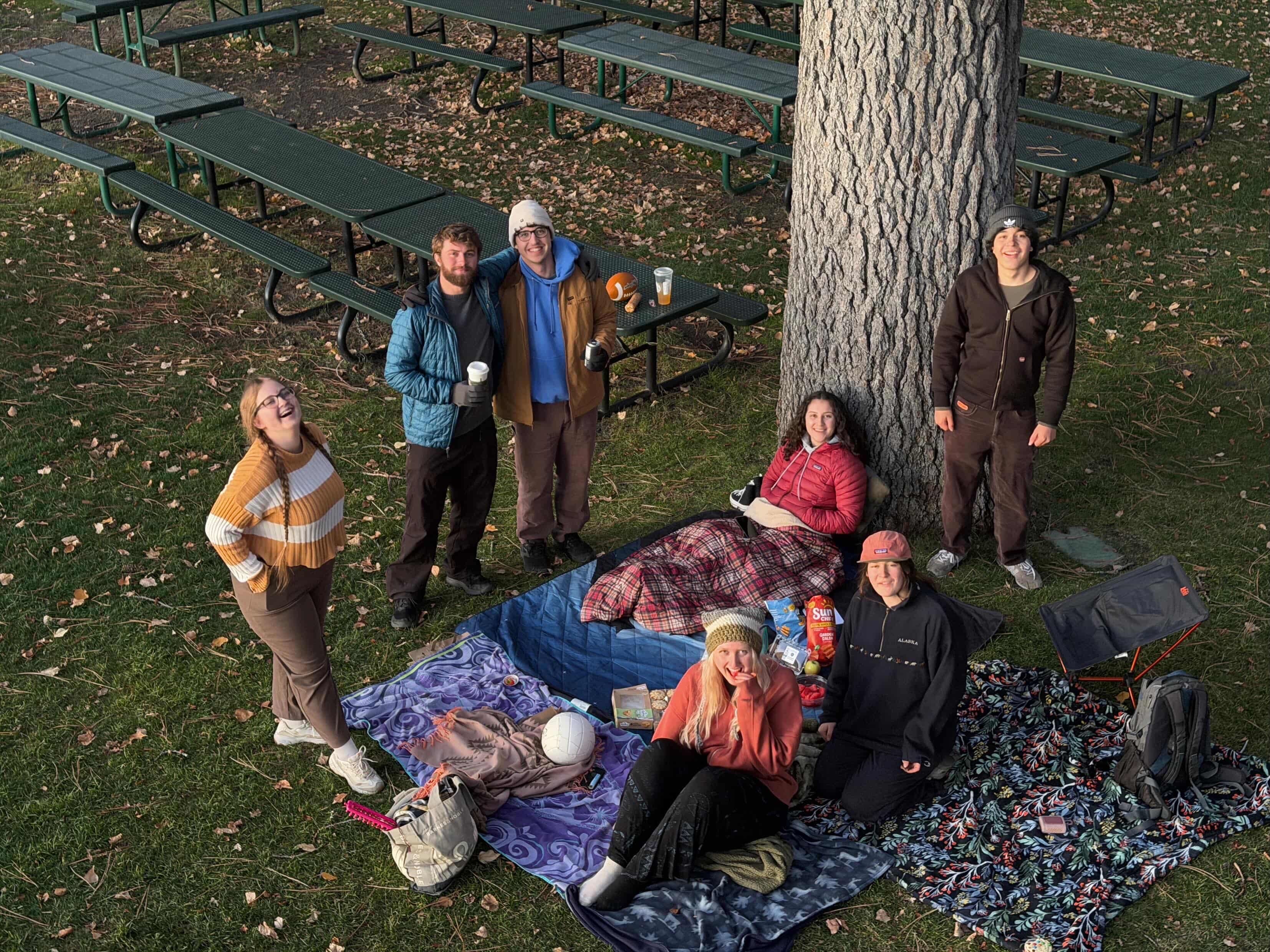 Students sit outside near trees having a picnic. 